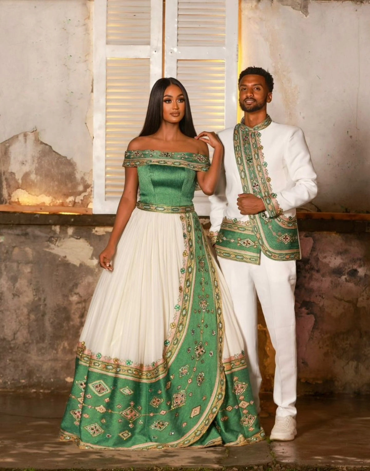 Man and woman in formal Ethiopian Traditional matching couple outfit with green and white outfits standing in a rustic setting.