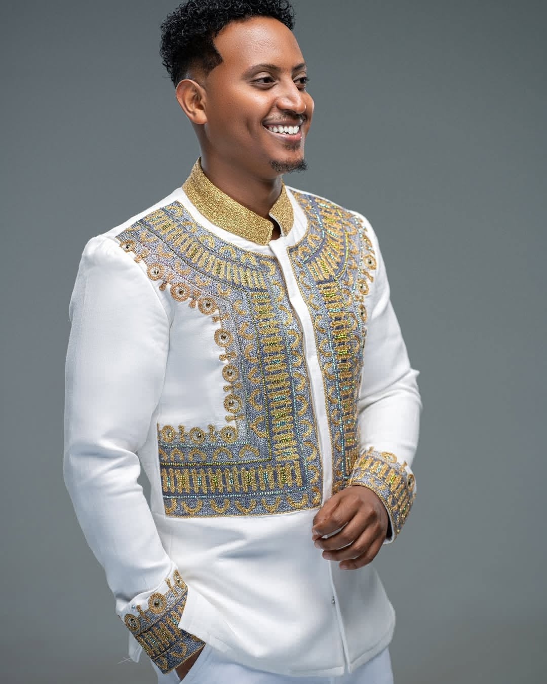 Man wearing Habesha Men’s Shirt  with gold and blue patterns on a gray background