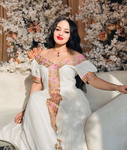 Woman in a white embroidered Ethiopian  Habesha dress sitting on a couch with floral decorations in the background