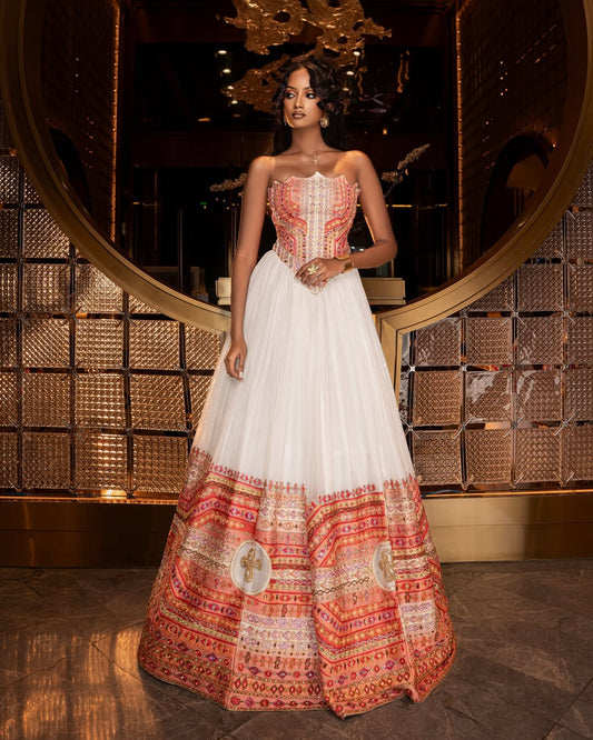 Woman wearing a traditional Ethiopian traditional dress  with a patterned top and white skirt in an elegant interior setting.