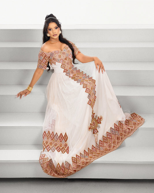 A woman models a white off-the-shoulder Ethiopian Traditional Clothing with intricate rust-orange and brown geometric embroidery, posing on light gray steps.