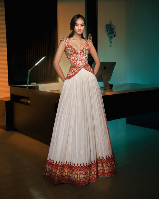 A woman models a traditional Indian evening Ethiopian National Dresses with a white pleated skirt, a heavily embellished red and gold beaded bodice, and a decorative red and gold border at the hem, set in a dimly lit modern office environment.