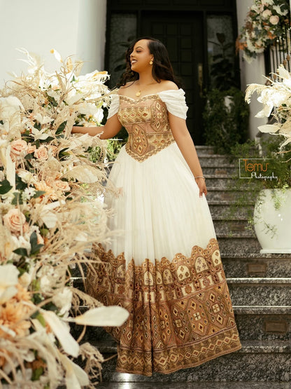 Woman in a white and gold Gold Ethiopian Wedding Dress standing on a decorated staircase with floral arrangements.
