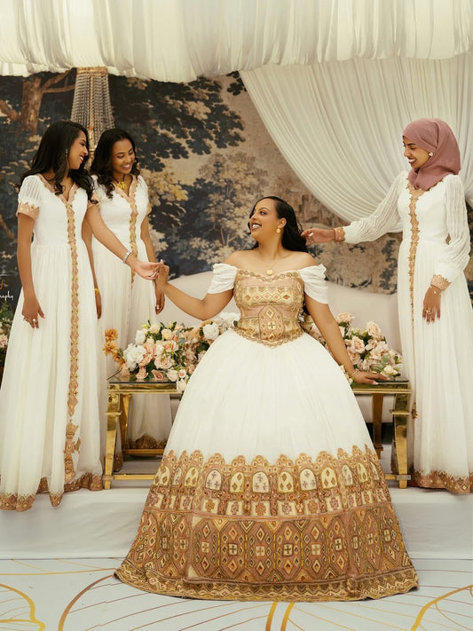 Woman in a traditional Gold Ethiopian Wedding Dress with gold embroidery, surrounded by three other women in white dresses.