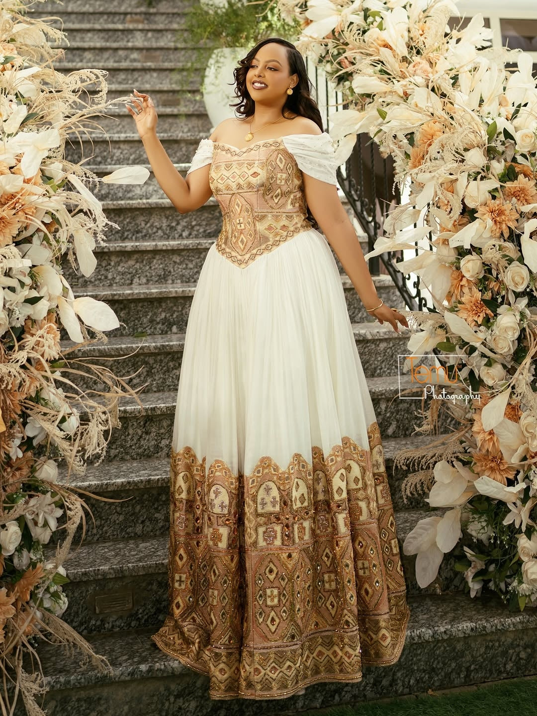 Woman in a white and gold embroidered Gold Ethiopian Wedding Dress standing on decorated stairs.