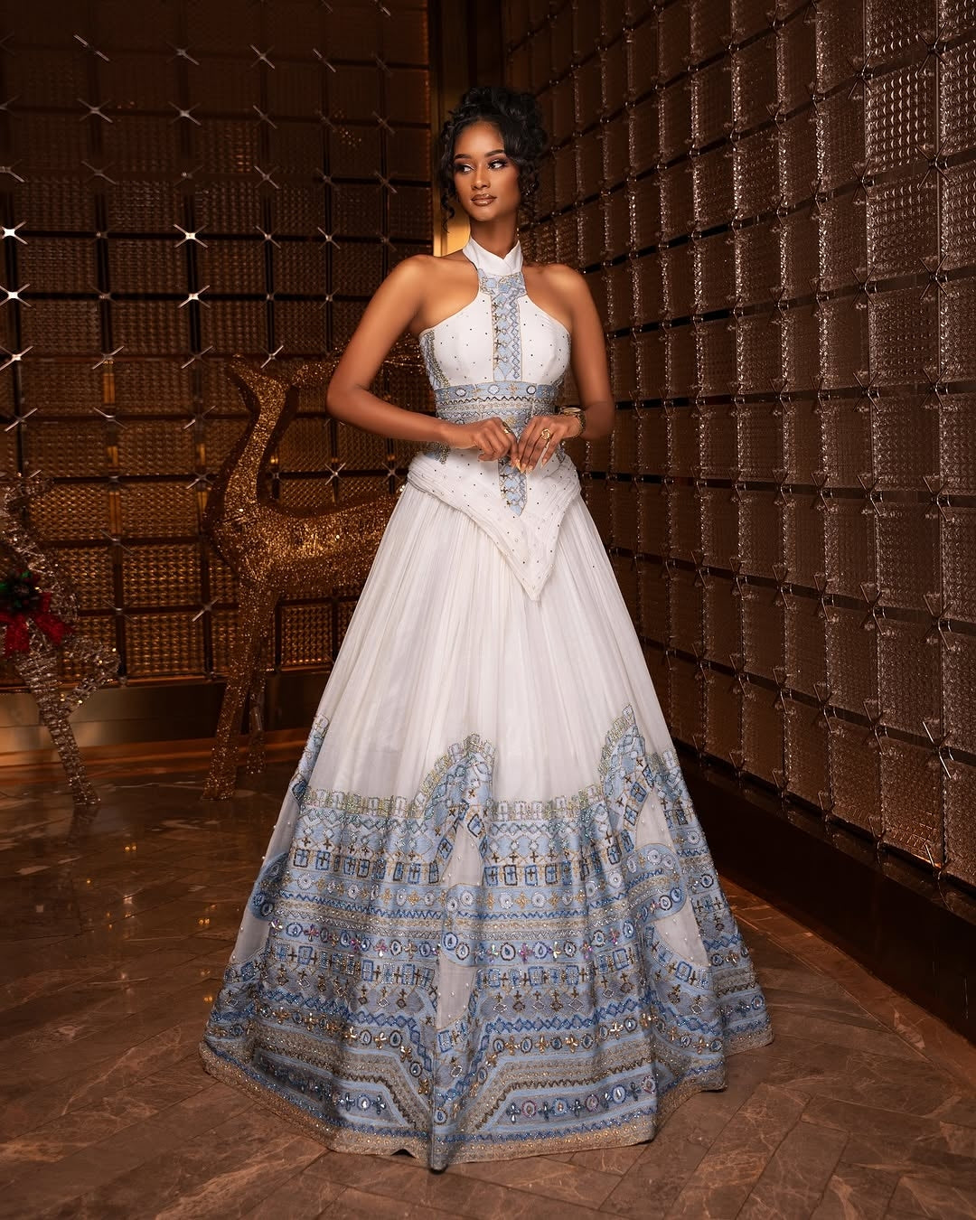 Woman in a white and blue patterned Blue habesha Wedding dress standing in a room with a textured wall.