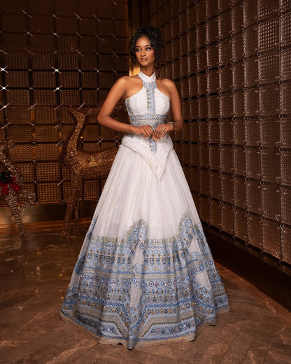 Woman in a white and blue patterned Blue habesha Wedding dress standing in a room with a textured wall.