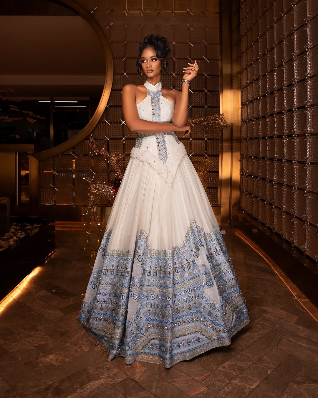 Woman in a white and blue patterned Blue habesha Wedding dress standing in a stylish interior setting.