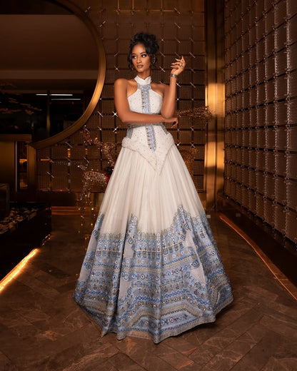 Woman in a white and blue patterned Blue habesha Wedding dress standing in a stylish interior setting.