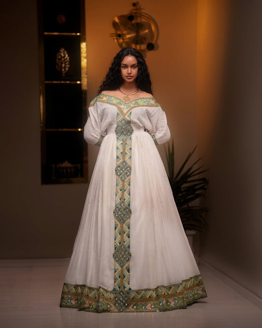 Woman wearing a white Green Ethiopian Dress with green and gold embroidery in an indoor setting.