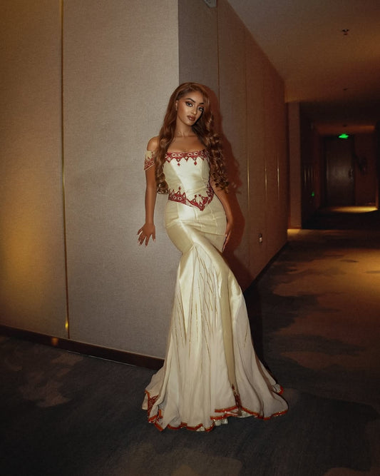 Woman in a white evening Red Eritrean Dress with red detailing standing in a dimly lit hallway.