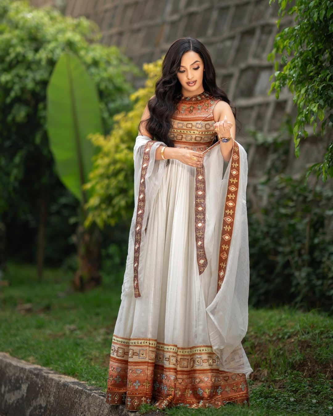 Woman in a Gold Habesha Kemis with a white and brown patterned dress standing outdoors.