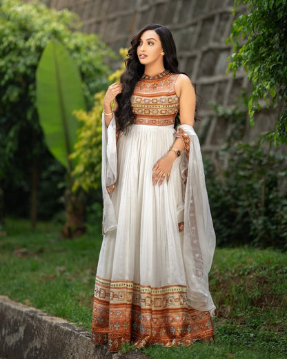 Woman in a Gold Habesha Kemis with a white and patterned dress standing outdoors.