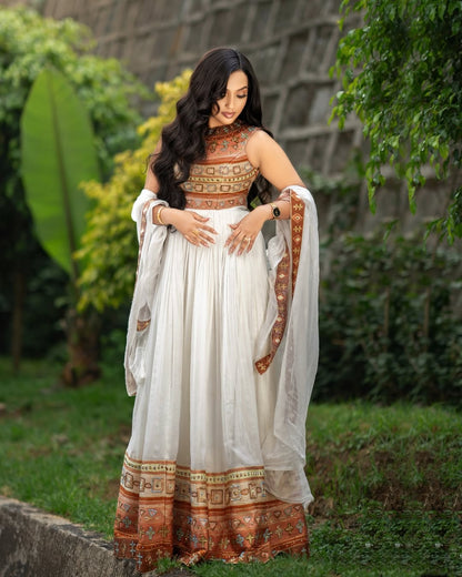 Woman in a traditional Gold Habesha Kemis with a white and patterned dress standing outdoors.