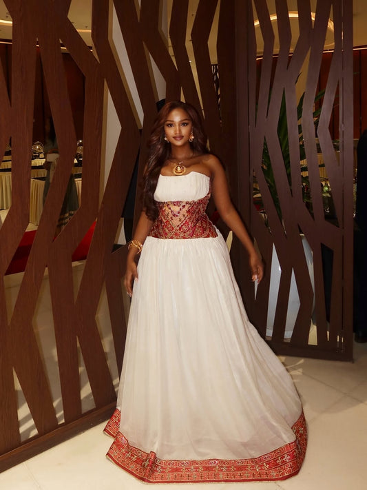 Woman in a traditional Ethiopian Traditional Dress standing in an indoor setting with decorative wall.