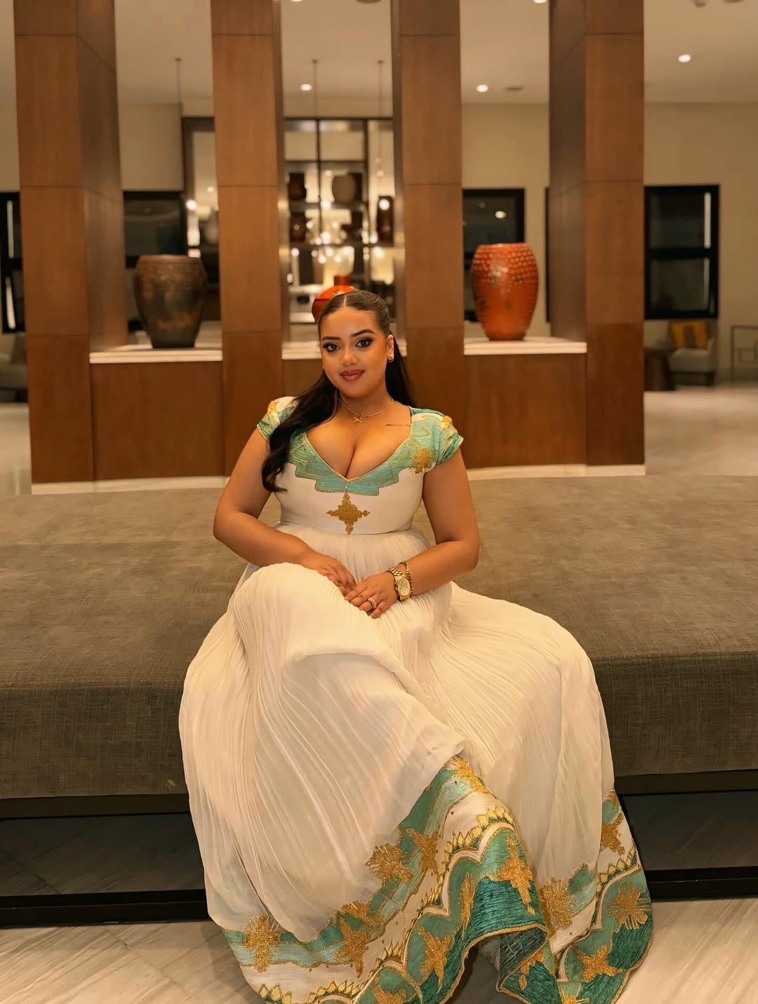 Woman in a white and Green Ethiopian Dress sitting in a modern indoor setting.