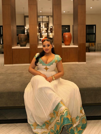 Woman in a white and Green Ethiopian Dress sitting in a modern indoor setting.
