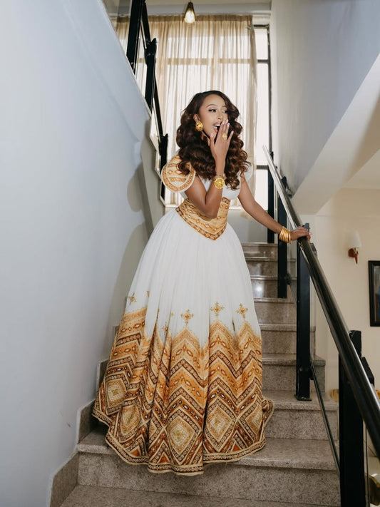 Woman in a white and gold patterned Royal Gold Habesha Wedding Dress standing on a staircase.
