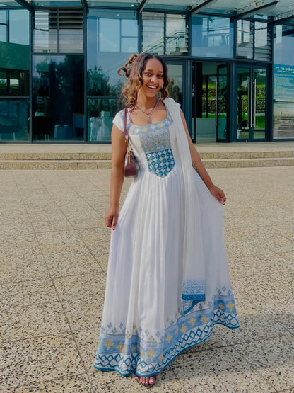 Woman in a white and blue Habesha Kemis standing in front of a modern building.