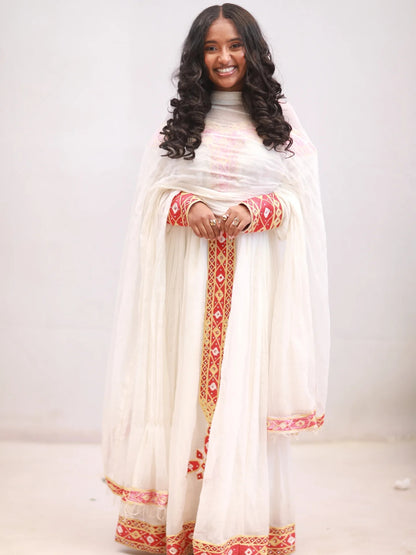 Woman wearing a white traditional Habesha kemis with red and gold patterns on a plain background