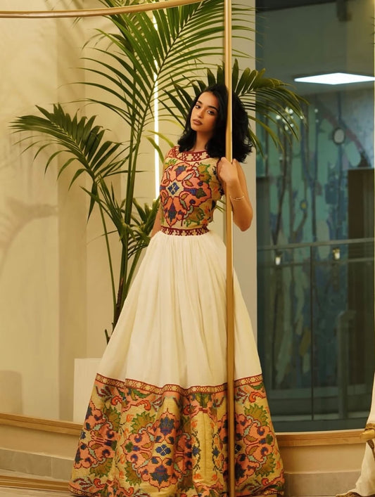 Woman in a colorful Ethiopian Traditional Dress standing in front of a mirror with plants in the background