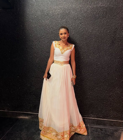 Woman in a white and gold Ethiopian traditional dress standing against a black wall.