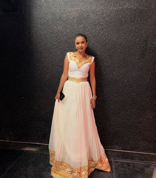 Woman in a white and gold Ethiopian traditional dress standing against a black wall.