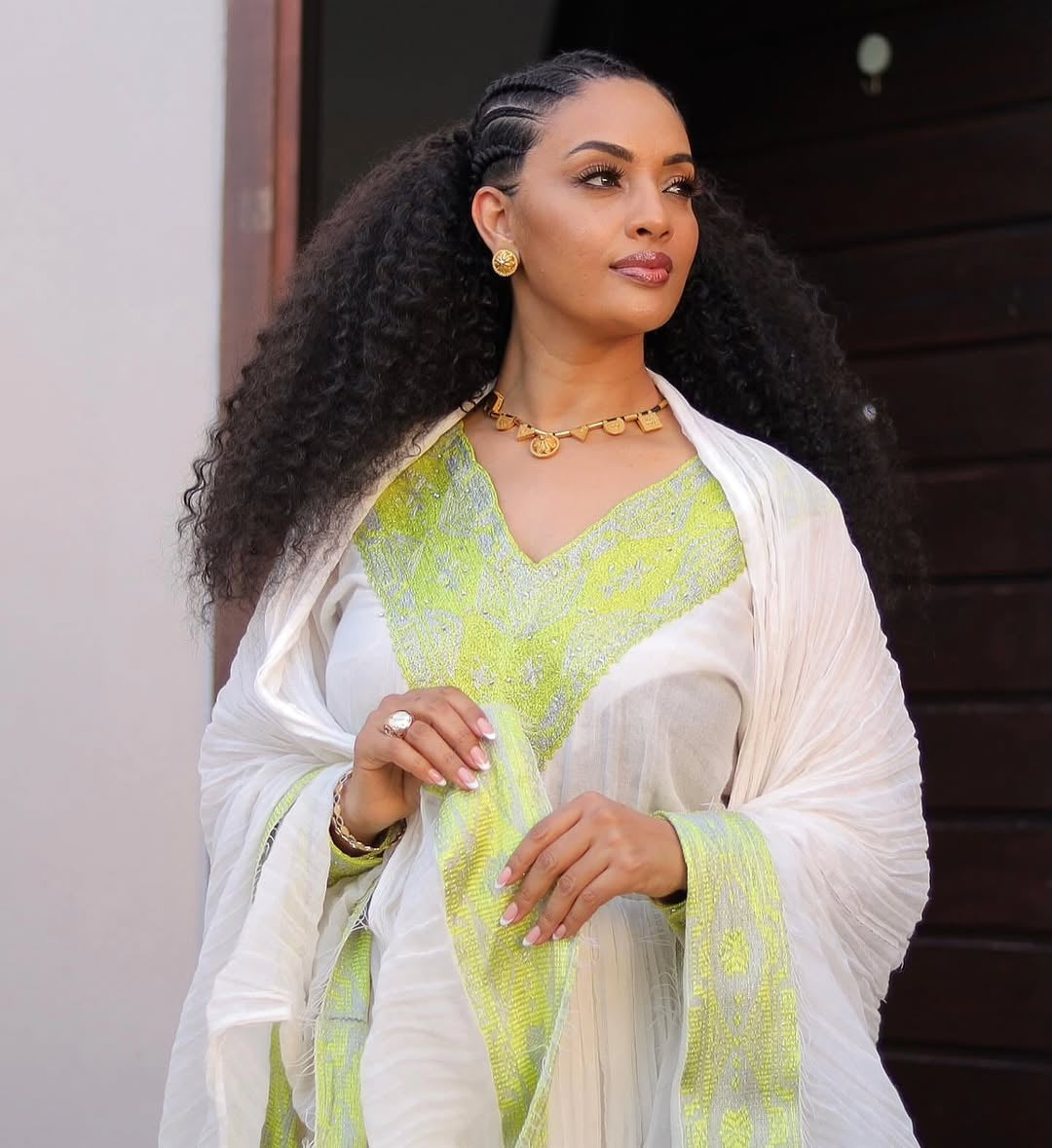 Woman wearing a green and white Habesha Dress with a white shawl.