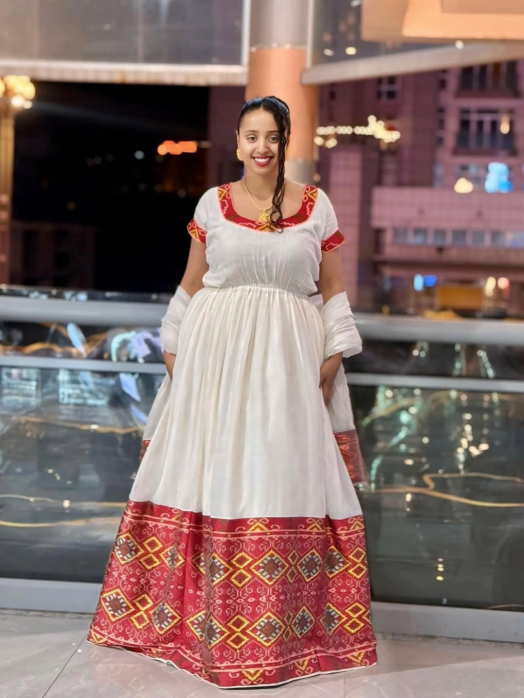 Woman wearing a white Ethiopian Dress with red and gold patterns in an indoor setting.