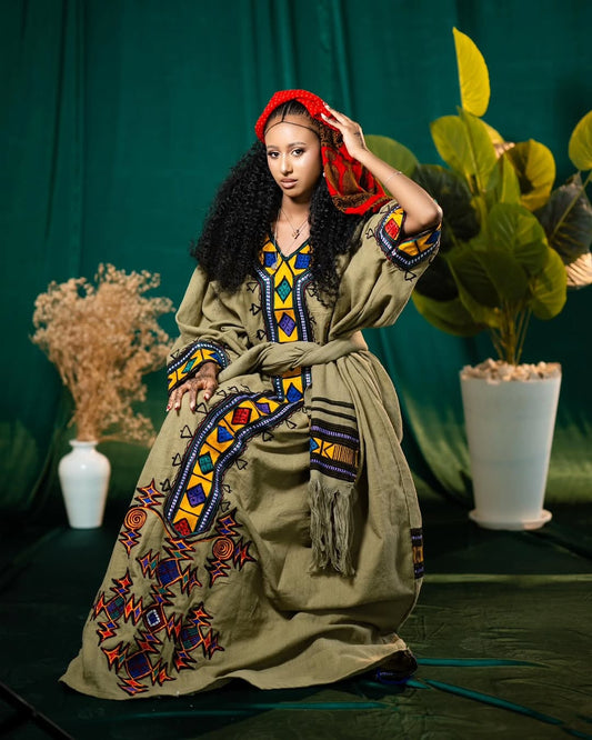 Woman in an embroidered Gonder Fetel Ethiopian Dress with a red headscarf against a green curtain background