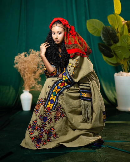Woman in Gonder Fetel Ethiopian Dress attire with a colorful headscarf and patterned dress against a green backdrop.