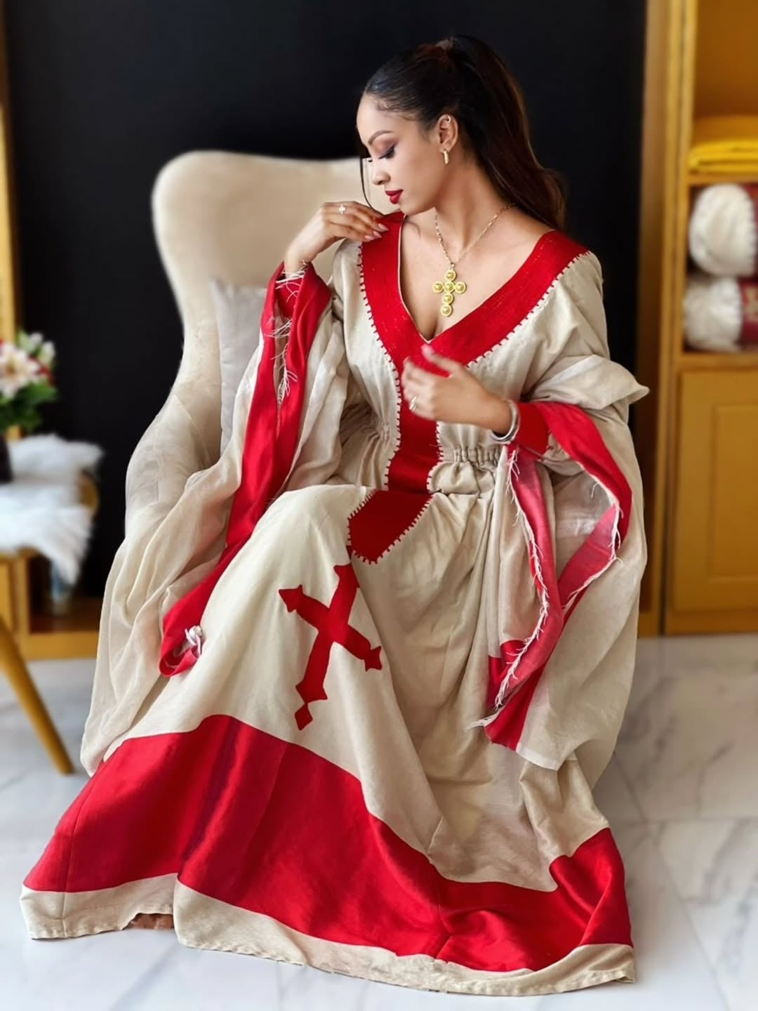 Woman in a historical costume with red and white Ethiopian traditional dress sitting on a chair.