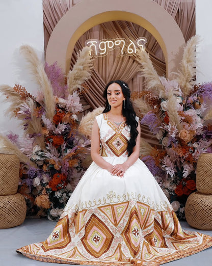 Woman in a white and gold embroidered wedding dress standing in front of decorative floral and wicker arch.