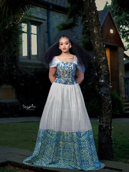 Woman wearing a white and blue patterned Ethiopian dress standing outdoors.