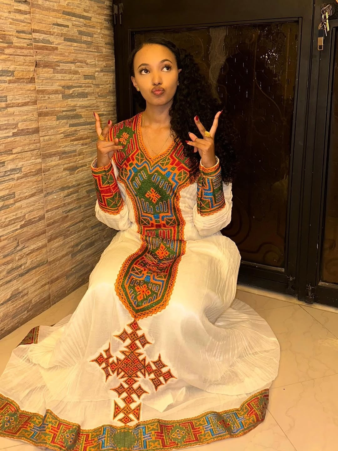 Woman in a colorful Habesha Libs sitting on the floor.