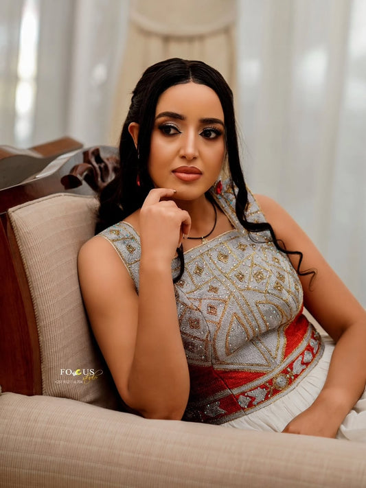 Woman in a traditional Red Habesha Kemis sitting on a couch with a neutral background