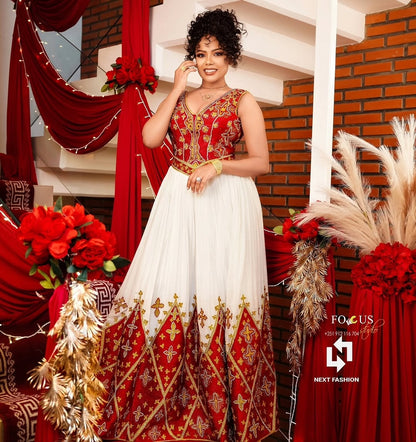 Woman in a red and white traditional outfit with gold embroidery, standing in a decorated indoor setting.