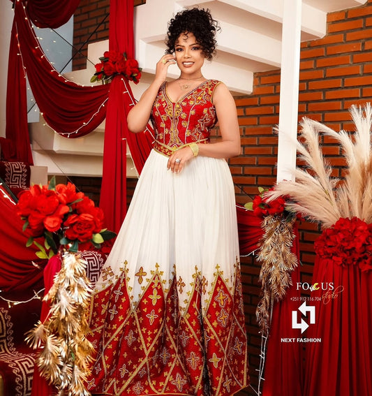 Woman in a red and white traditional outfit with gold embroidery, standing in a decorated indoor setting.