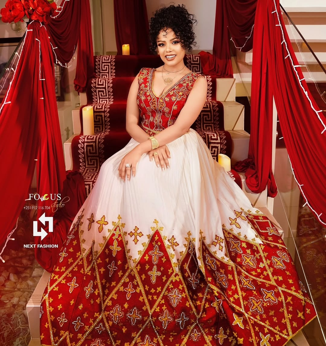 Woman in a red and Ethiopian Bridal Dress embroidered traditional outfit sitting on a decorated chair.