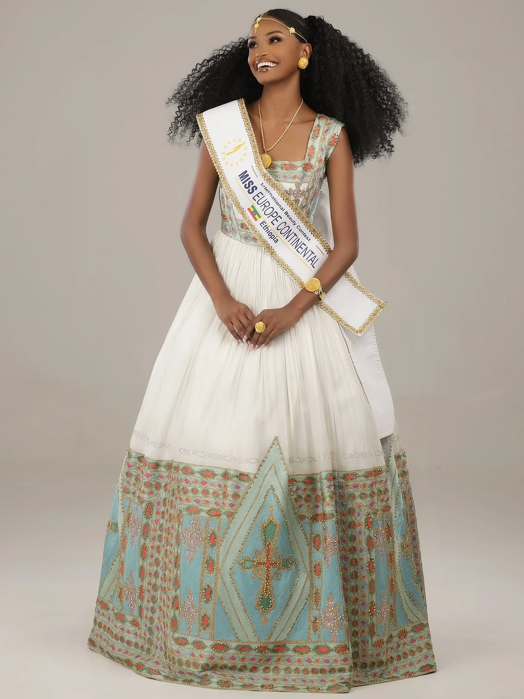Woman in a formal Eritrean Libs  holding a sash with 'Miss Euphoria Centennial' on a plain background