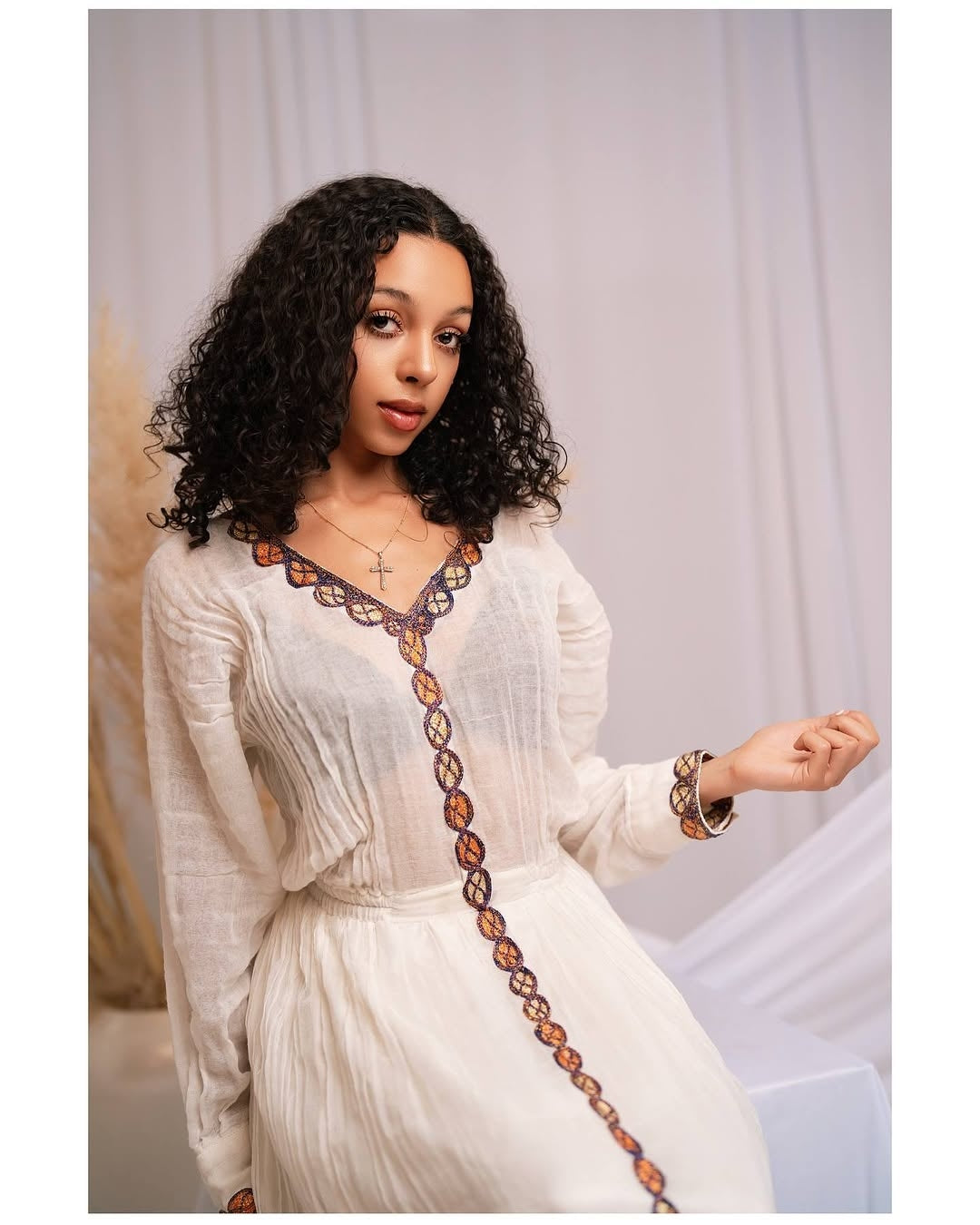 Woman wearing a white Red Habesha Dress with a decorative brown trim against a plain background