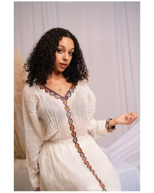 Woman wearing a white Red Habesha Dress with a decorative brown trim against a plain background