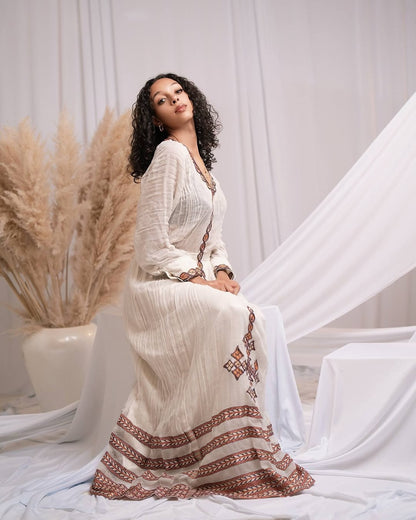Woman in a white dress with red patterns sitting in a decorative setting with pampas grass.
