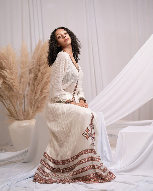 Woman in a white dress with red patterns sitting in a decorative setting with pampas grass.