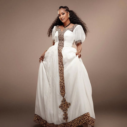 Woman wearing a white Habesha Kemis with brown embroidery against a brown background