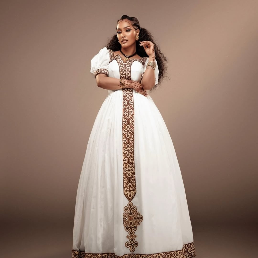 Woman wearing a white Habesha Kemis with gold embroidery against a brown background