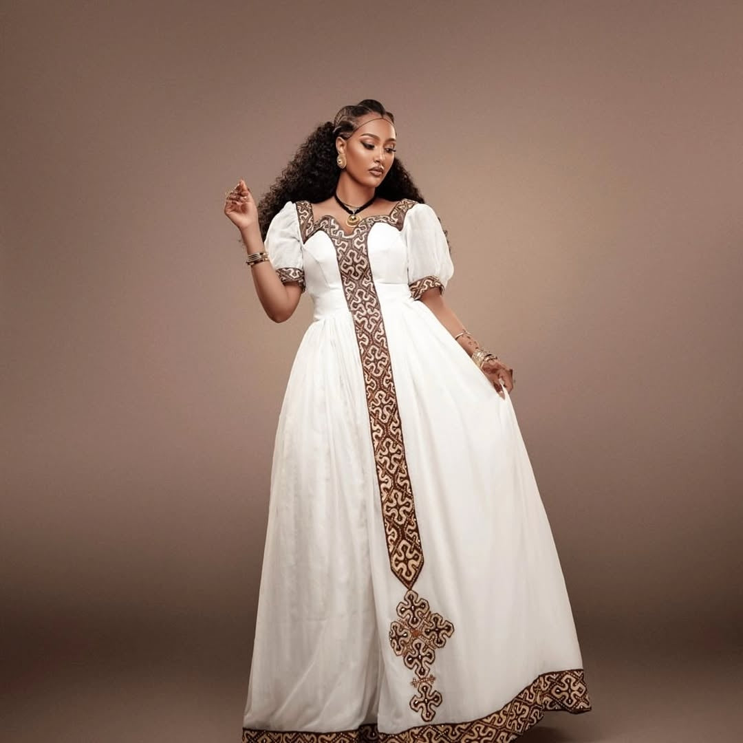 Woman wearing a white Habesha Kemis with brown embroidery against a brown background