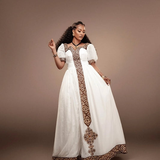 Woman wearing a white Habesha Kemis with brown embroidery against a brown background
