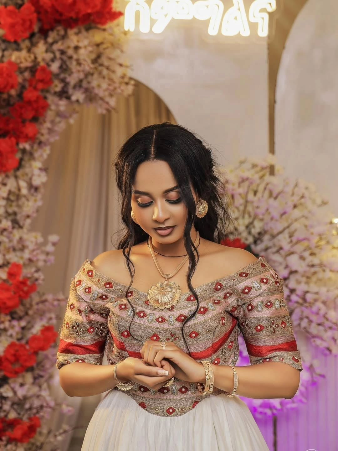Woman in an embroidered Habesha Wedding  Dress with floral decorations in the background