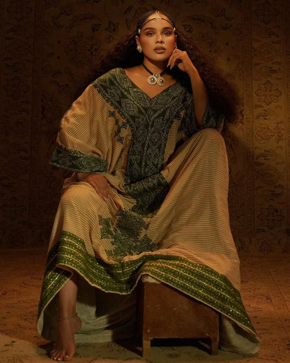 Woman in Gondar Fetel attire sitting on a wooden stool against a textured wall.